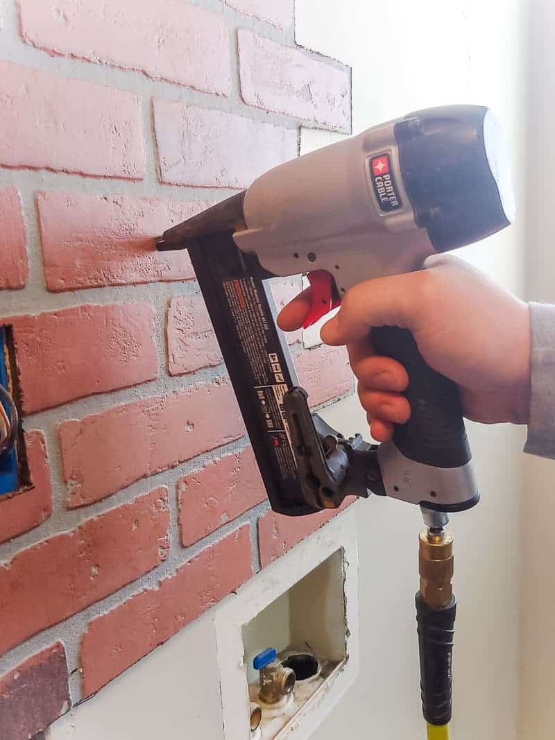 Man attaching fake brick paneling to the wall with a staple gun 