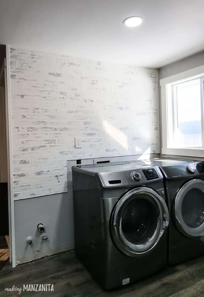 German schmear faux brick wall above washer and dyer in modern farmhouse laundry room with window