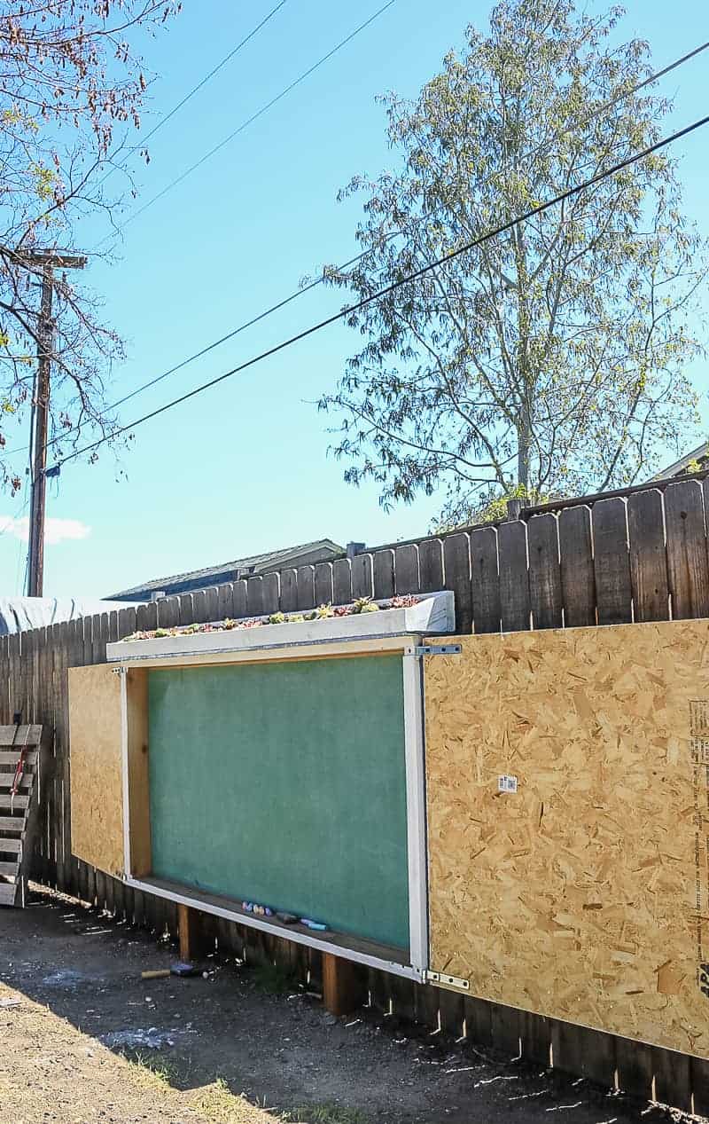 A side view of our large outdoor chalkboard in our backyard fence! The chalkboard hangs on the fence and has a fun "live roof" succulent planter along the top.