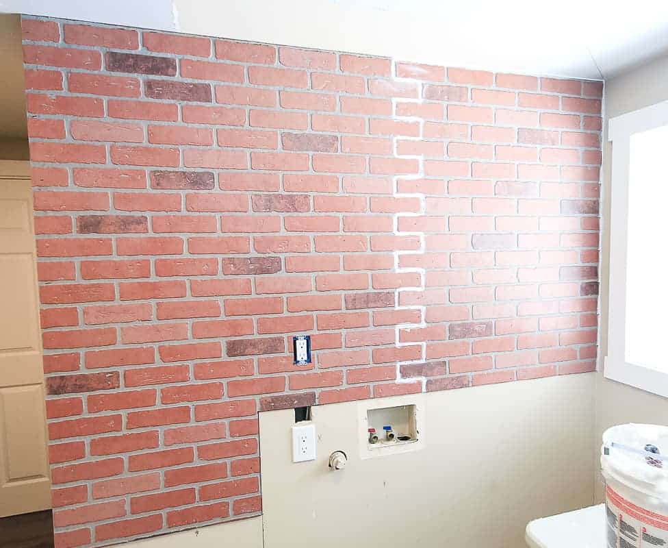 Faux brick wall panels attached to a wall in laundry room and cut to fit together to hide the seam and then filled with caulking before applying the german schmear treatment 