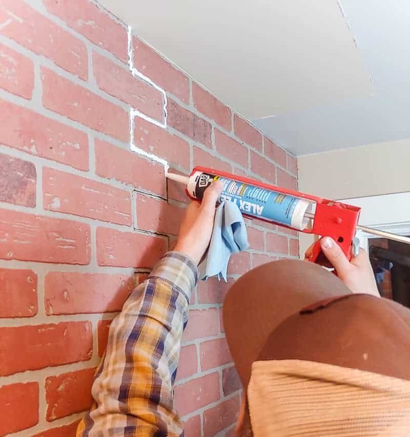Man caulking the joint between two faux brick wall panels with DAP Alex Flex caulk