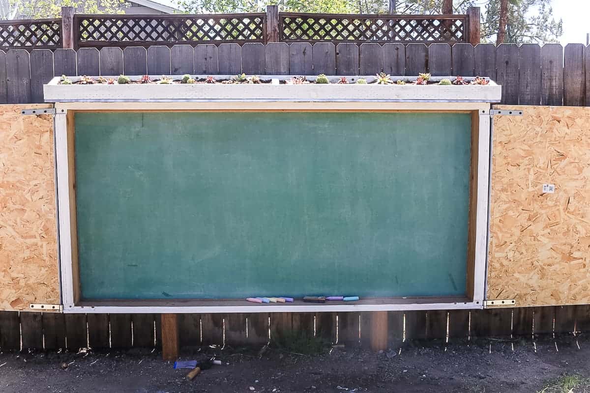 A front view of our large outdoor chalkboard! This chalkboard is hangs on the fence, housed in a large protective box, with a live roof planter box filled with succulent plants.