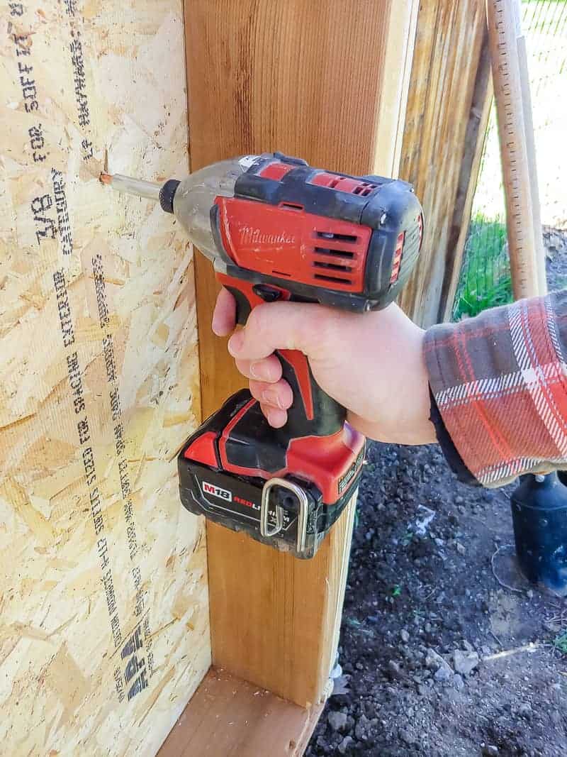 Using an electric drill, attach the outdoor chalkboard box to the support beam attached the the fence.