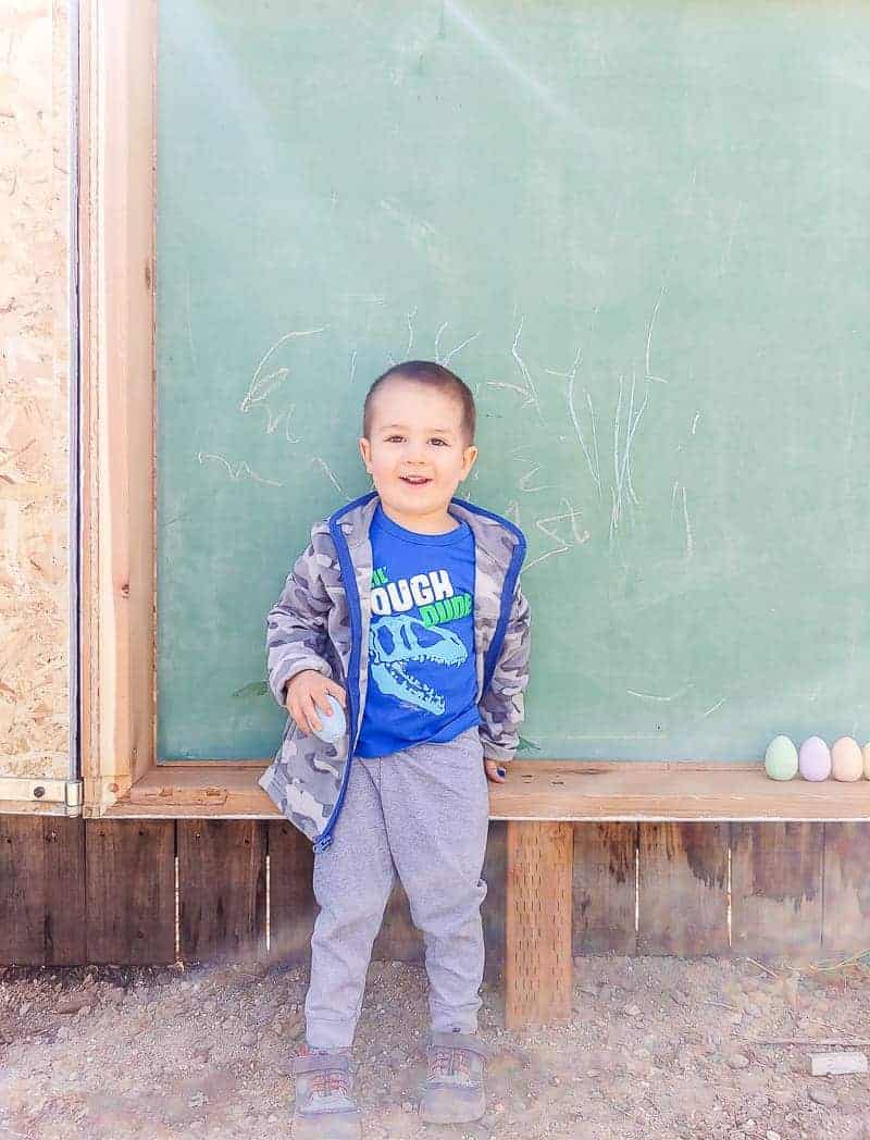 Cal stands in front of his new favorite toy - our large outdoor chalkboard - proudly holding chalk eggs and drawing on the board.