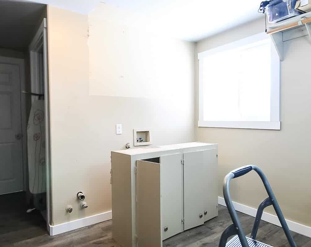 Laundry room makeover in progress with upper cabinet removed and set on floor where the washer and dryer goes in laundry room