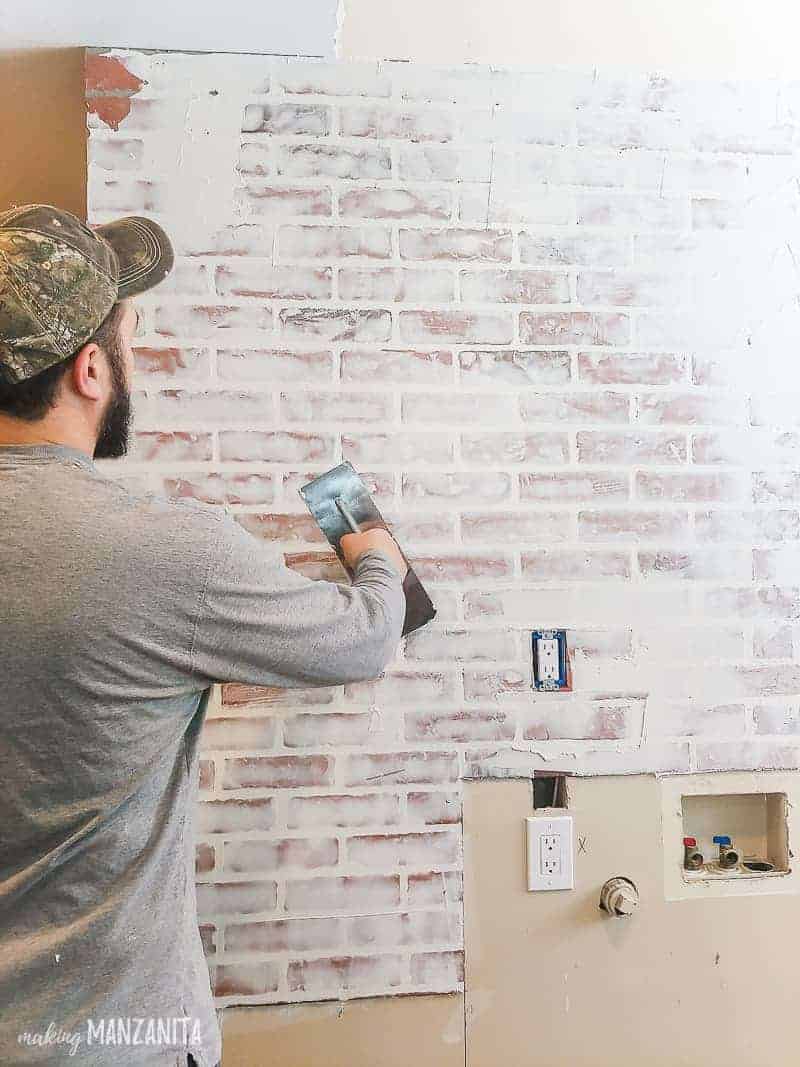 Man applying joint compound with a trowel over fake brick wall paneling to create a german smear finish 