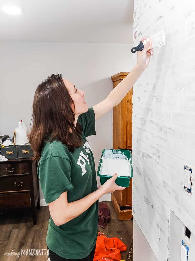 Woman painting fake brick wall panels with watered down white paint to seal german schmear treatment 