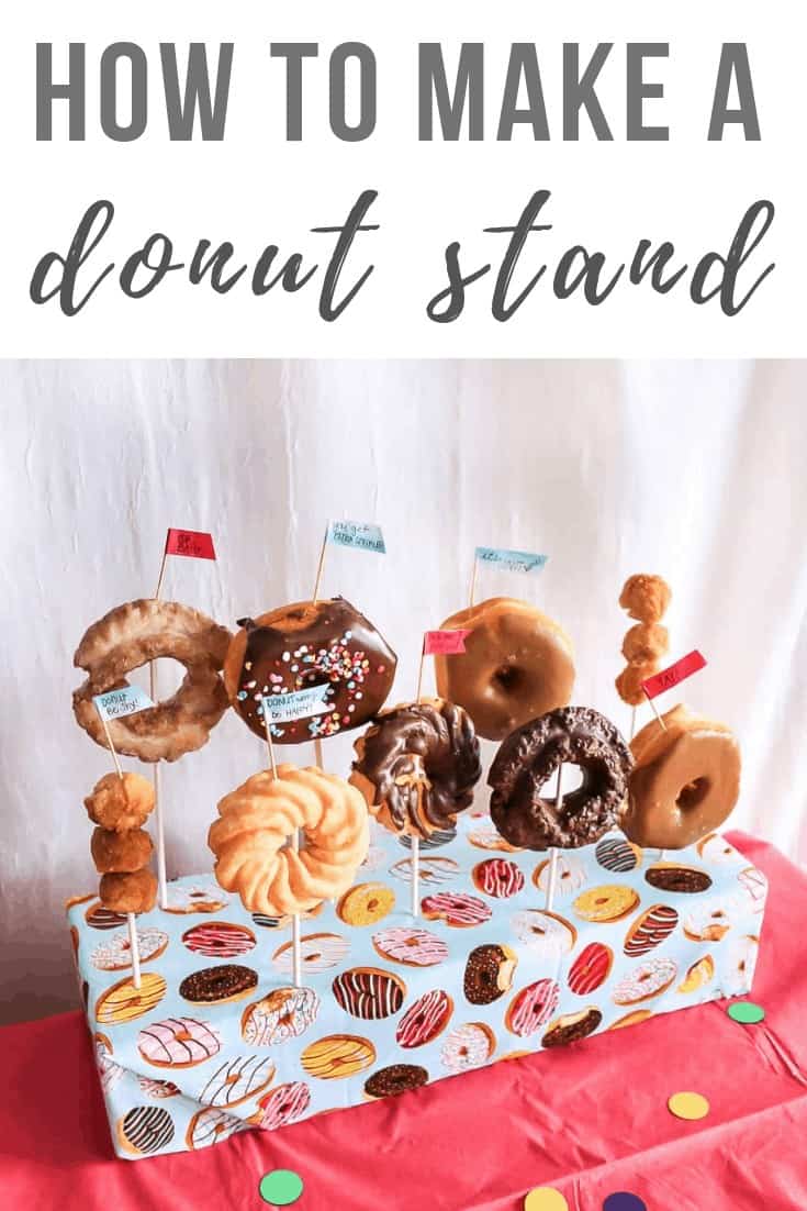 DIY donut stand with donuts standing on sticks with tiny statement flags on top of the table with text overlay that says How to Make a Donut Stand.