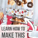 Donut stand in the center of the party food like orange juice, cups and stirrers, mixed berries and spoons on top of the table with text overlay that says Learn How to Make this Donut Stand.