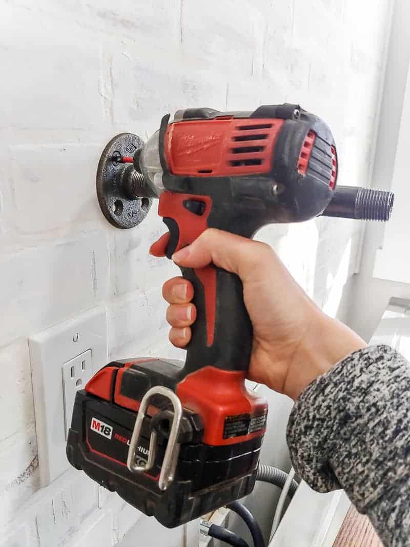 Add the pipe bracket for the industrial pipe shelf to the wall using a drill