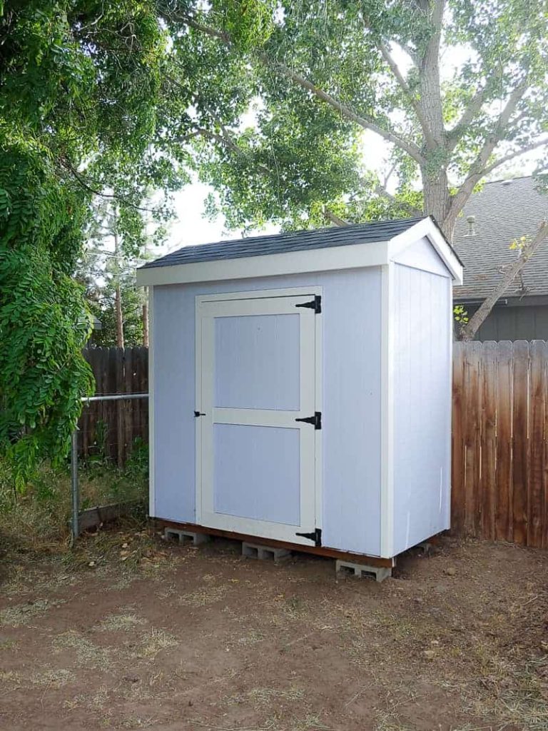 shows a picture of a light blue garden shed next to the back fence in backyard 