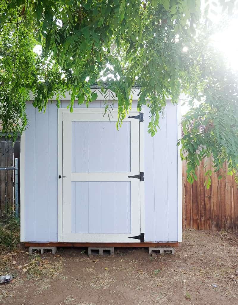 Full image of a white farmhouse garden tool storage with tree leaves hovering over.