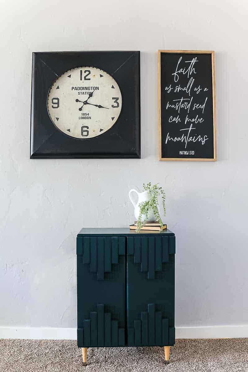 Full image of dark green aztec style laminate cabinet makeover with tribal pattern with clock and frame above and farmhouse decor on top of it.