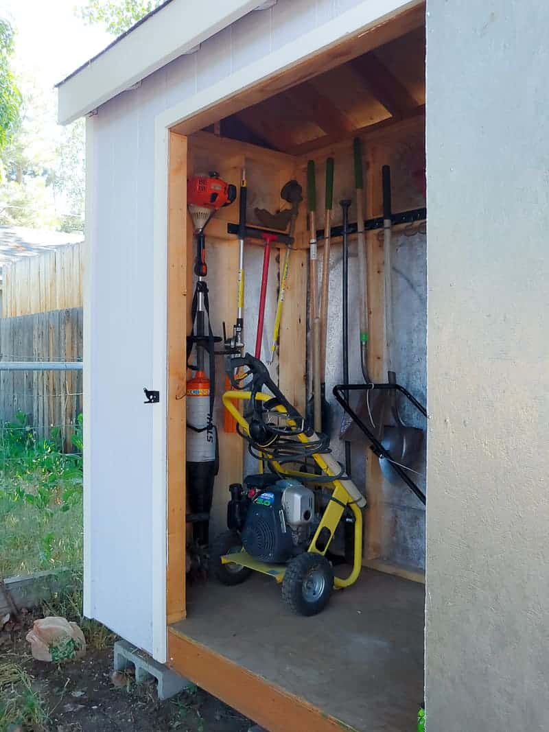 Side view of garden tool storage - the shed door is open, showing the organized garden tools in a wall mounted system and other garden machines