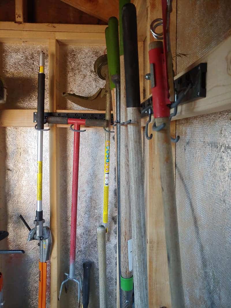A closer look at our garden tools storage solution: wall-mounted hooks hold our gardening tools by the handles, keeping them organized and off the ground.