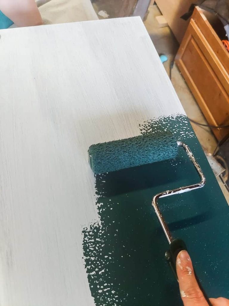 Painting the top of the cabinet with dark green paint to transform it using a roller a boho laminate cabinet makeover.