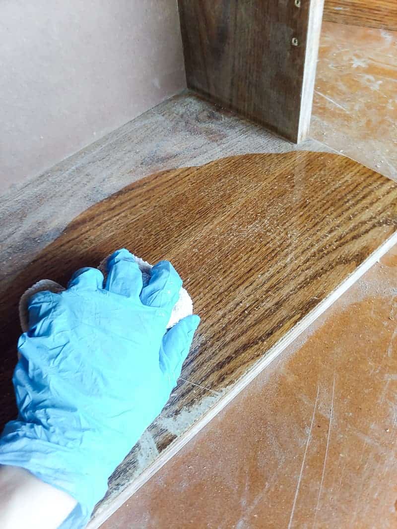 Hands wearing gloves wiping the sanded cabinet with wet cloth and TSP on a laminate cabinet makeover.