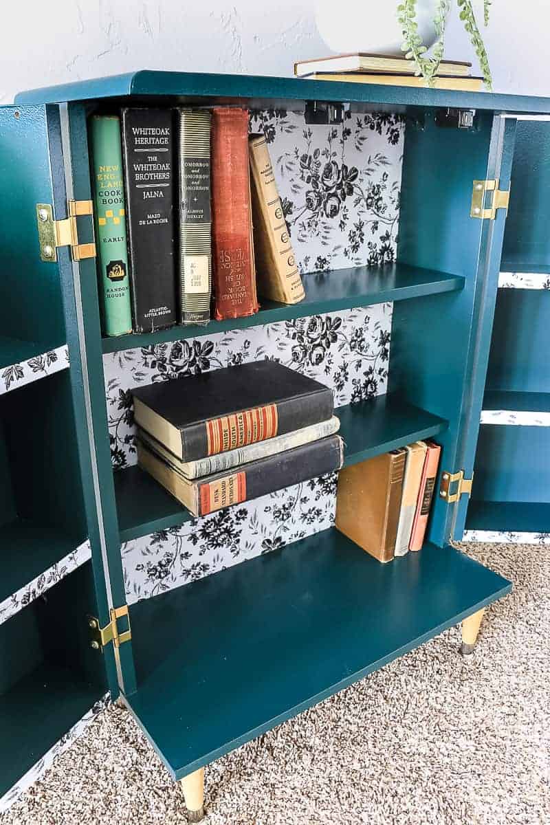 Opened dark green boho style laminate cabinet makeover showing the inside with vintage books on the shelves.