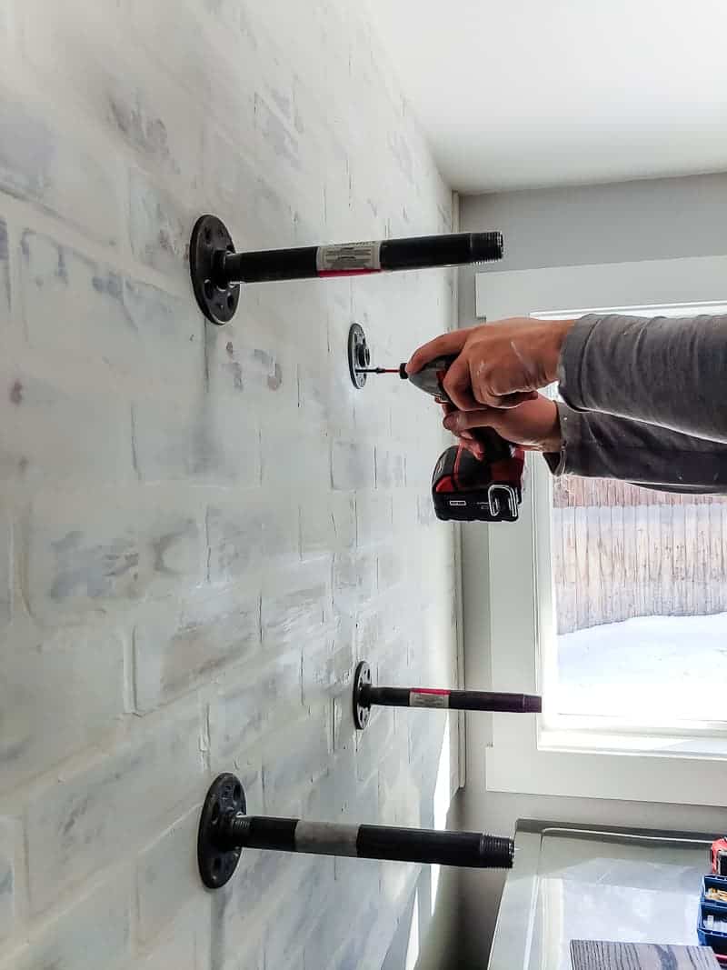 Adding two sets of pipe brackets to the wall to create the base for industrial pipe shelving