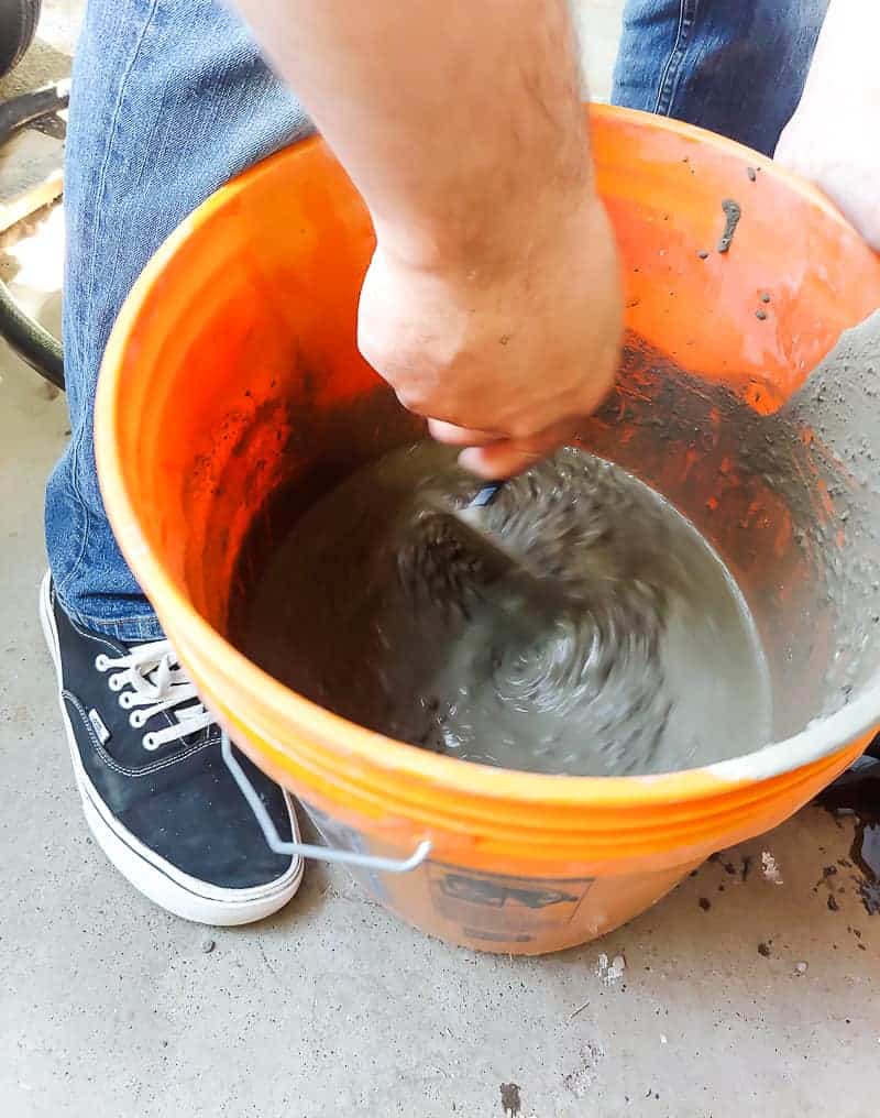 Hand mixing the concrete mix in an orange bucket to create the DIY garden stepping stones