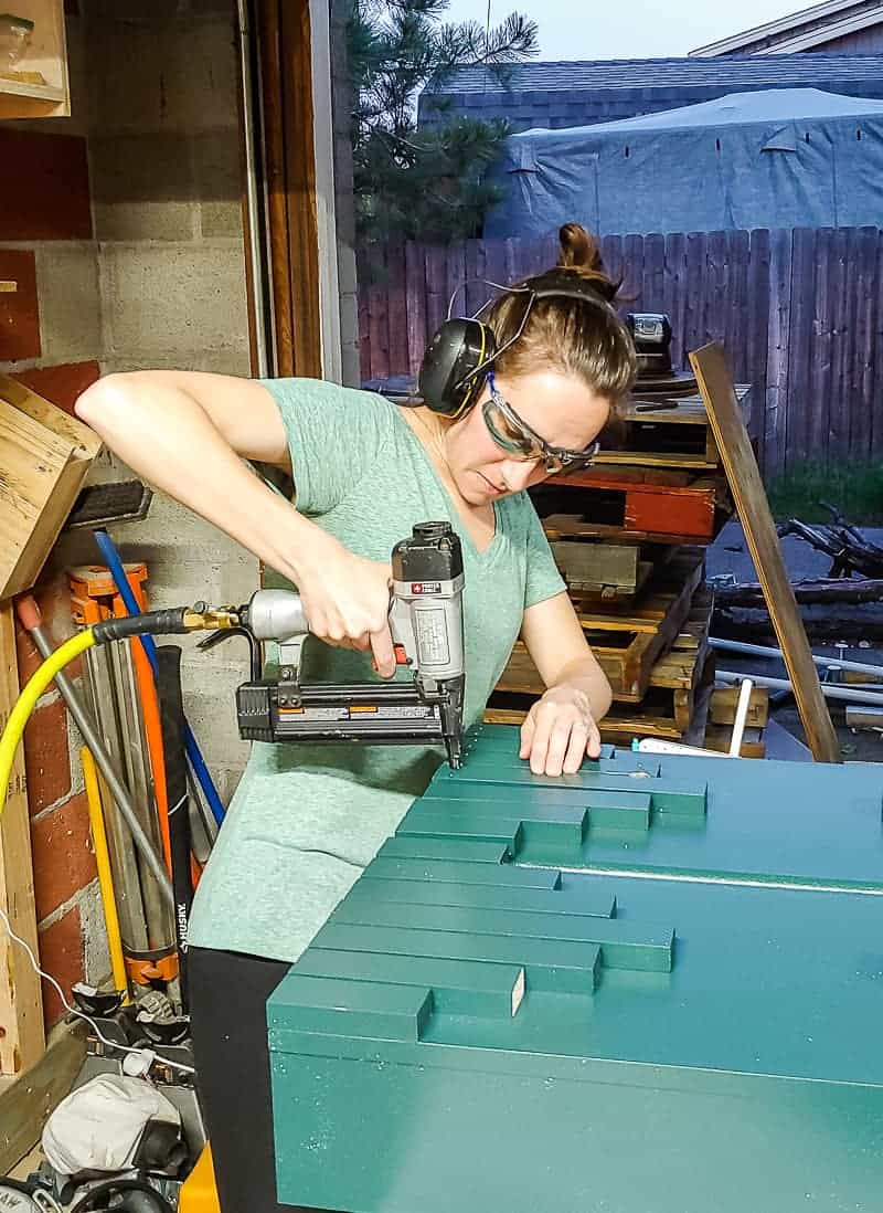 Woman in headphones wearing safety glasses attaching the trim pieces onto the laminate cabinet makeover.