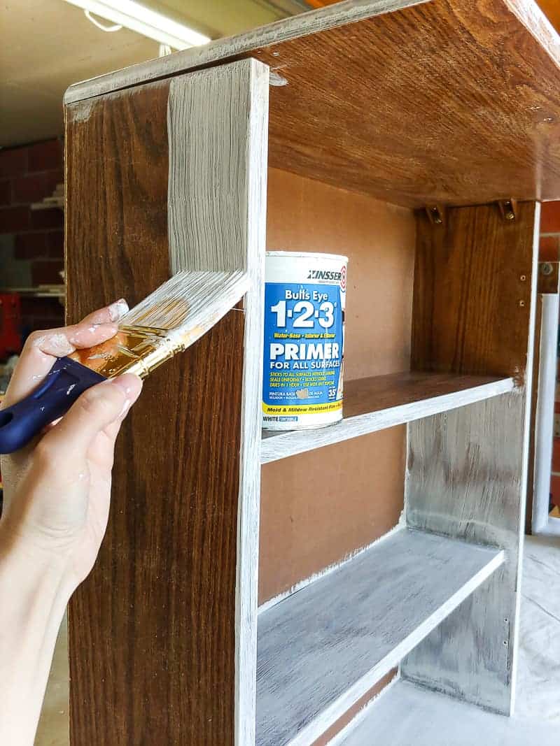 Painting cleaned cabinet with primer using paint brush on a laminate cabinet makeover.