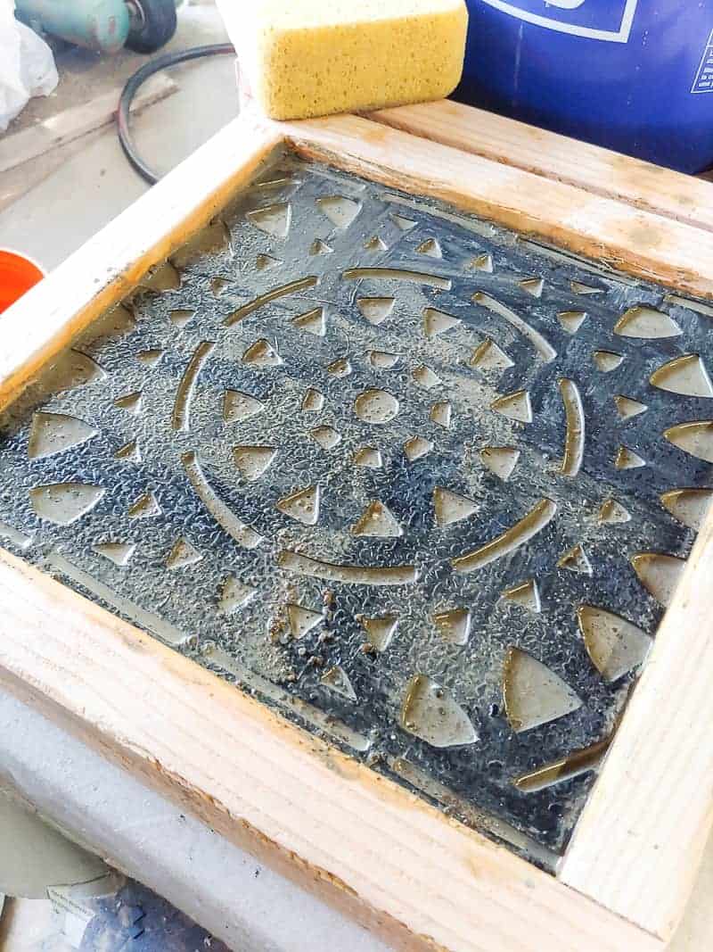 A cut piece of rubber doormat sitting in wet concrete to make DIY garden stepping stones