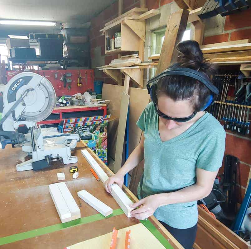 woman in headphones and safety glasses measuring trim pieces for cutting a laminate cabinet makeover.