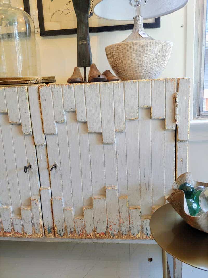 White vintage boho style cabinet with farmhouse home decor above it. The before photo of laminate cabinet makeover