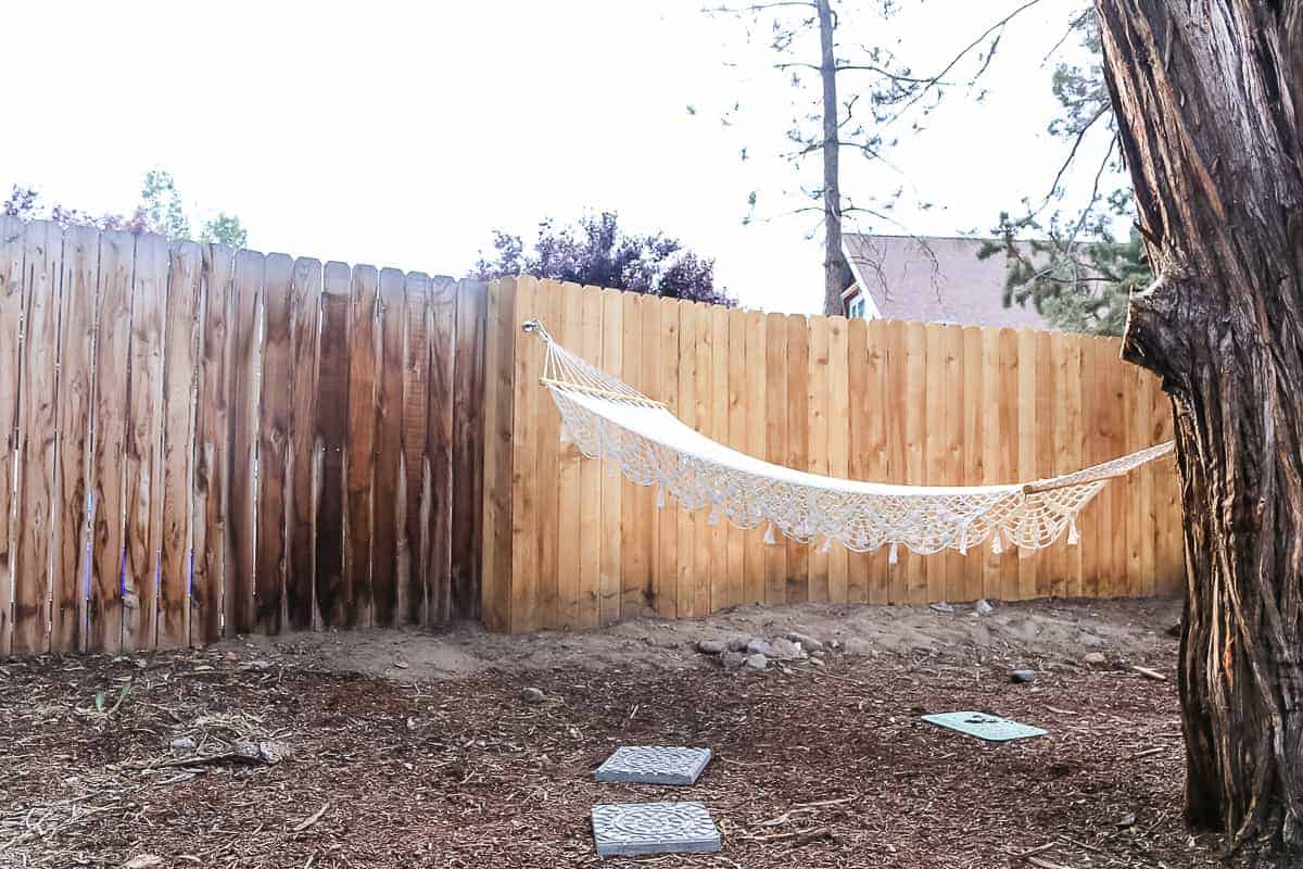 Two concrete garden stepping stones on the ground with a hammock hanging from the fence and a tree.