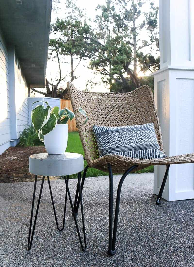 A DIY concrete side table on our backyard patio paired with a woven wicker chair with matching hairpin legs