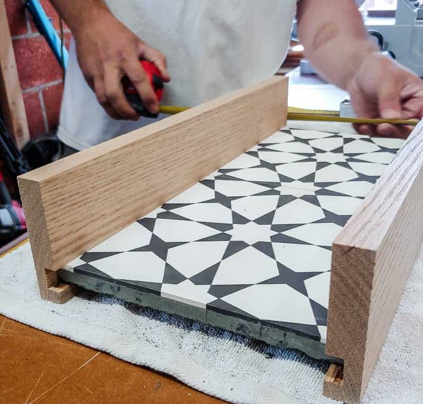 what to do with leftover tiles. Cement tiles with wood on each side and man measuring the other sides of the diy serving tray