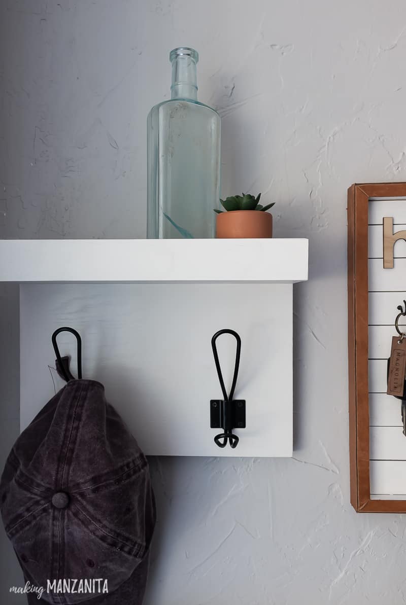 Hanging shelf with hooks and a farmhouse bottle and succulent on top of the shelf