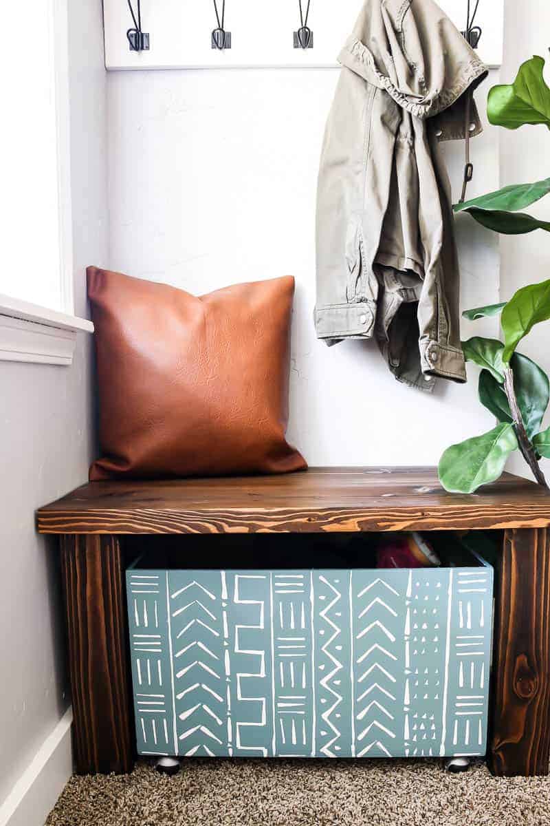 Leather pillow, wooden bench and wooden storage and coat hanging on the coat rack in entryway