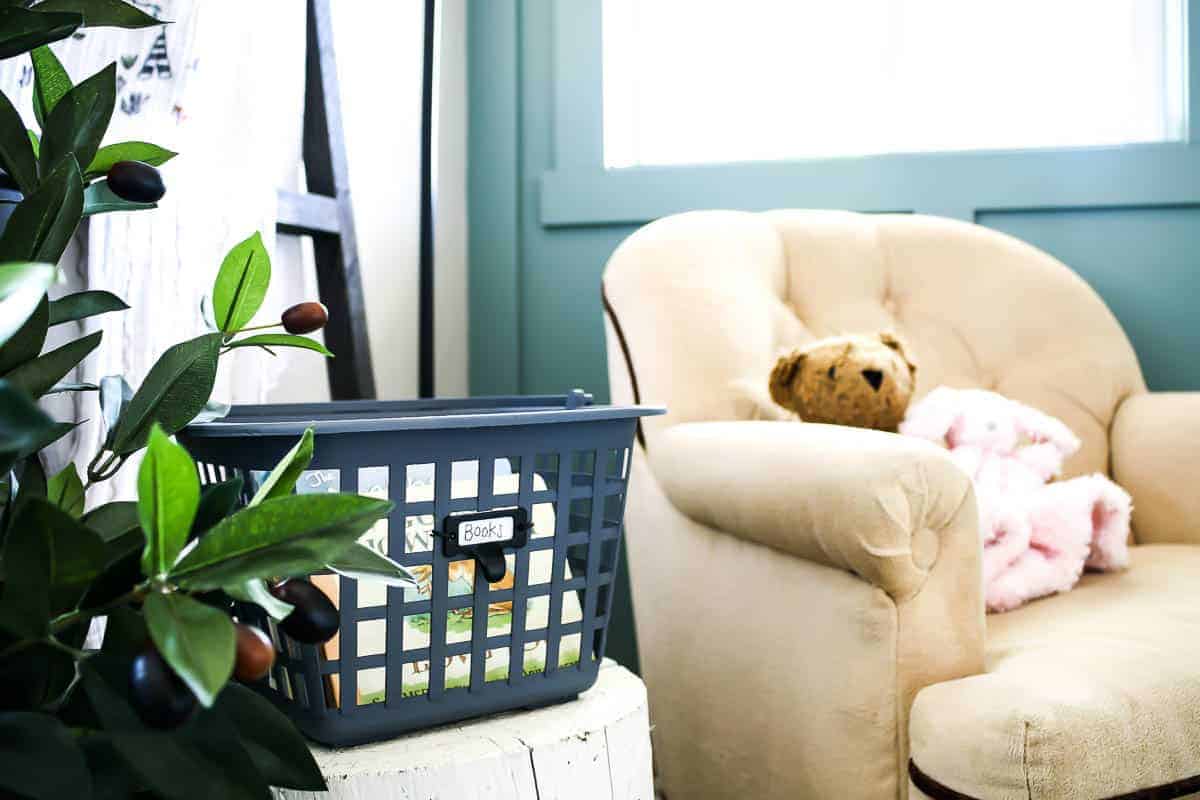 A DIY book basket sits on a bedside table, next to a vintage tan suede rocking chair in our baby girl's boho style nursery. 
