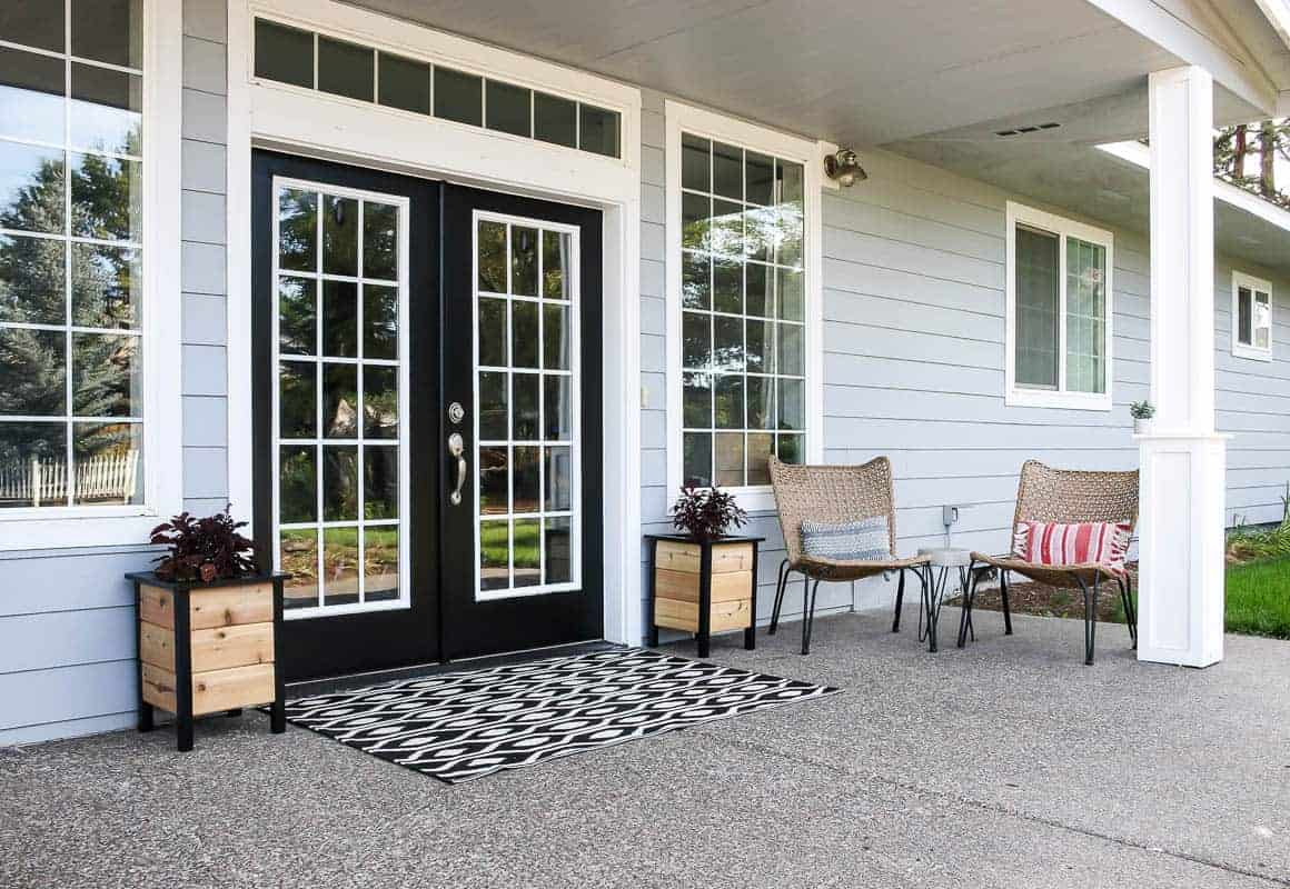 Our new front porch decor! Two DIY planter boxes frame the front door, along with a black and white outdoor rug, two wicker chairs, and a DIY concrete side table.