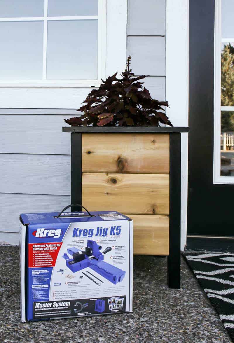 A finished DIY planter box - cedar wood planks framed with black painted wood legs - pictured with the Kreg Jig K5 system, the tools we used to make this planter box.