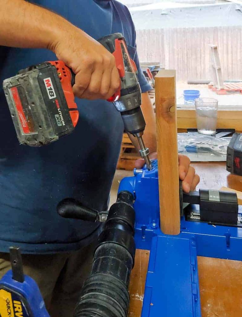 A man is seen using a drill with a Kreg Jig to create pocket holes in the wood.