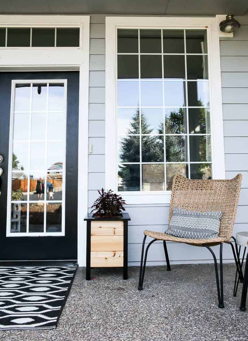 A look at one side of our front porch - one DIY planter box - natural cedar wood plants with black frame and legs, and a wicker chair with hairpin legs.