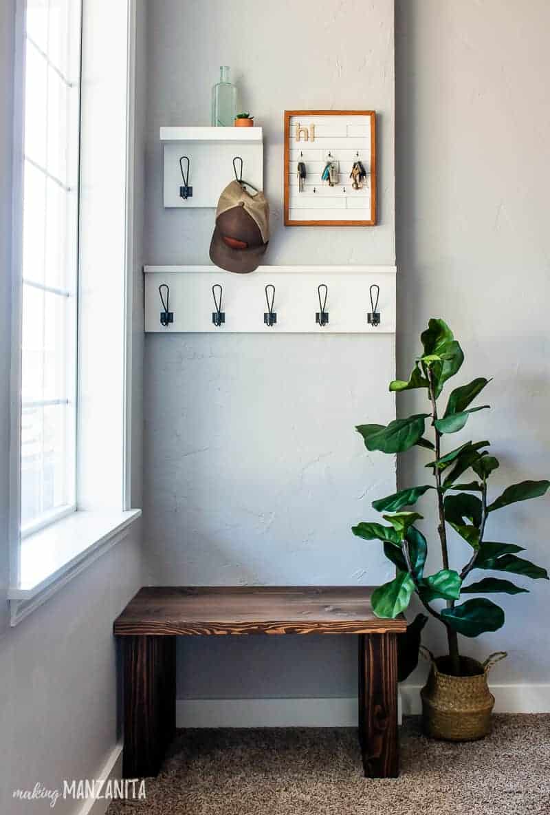 Small entryway with the racks, key holder, modern wood bench and an indoor plant 