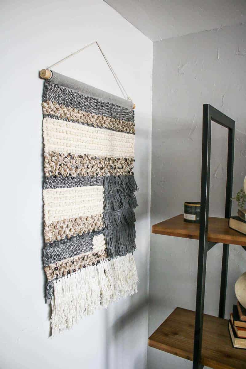 This farmhouse style woven wall hanging doesn't necessarily count as living room shelf decor, but complements the living room bookshelf perfectly with neutral tones.