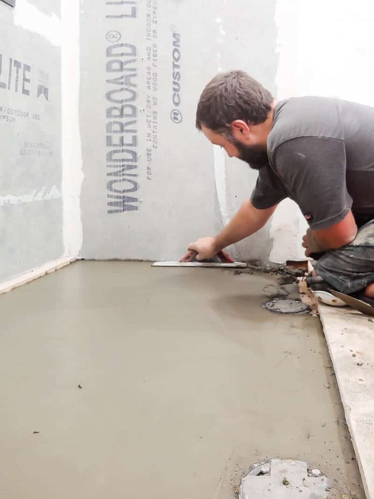 There is a man flattening cement to the floor to create a shower base. 