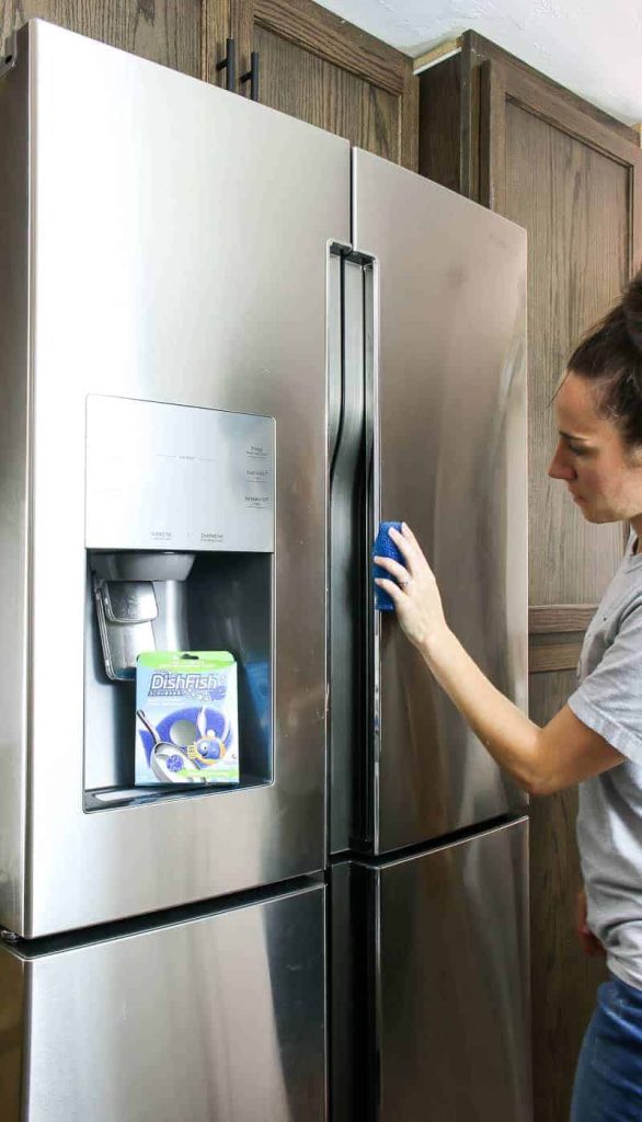 Cleaning outside of stainless steel fridge with sponge