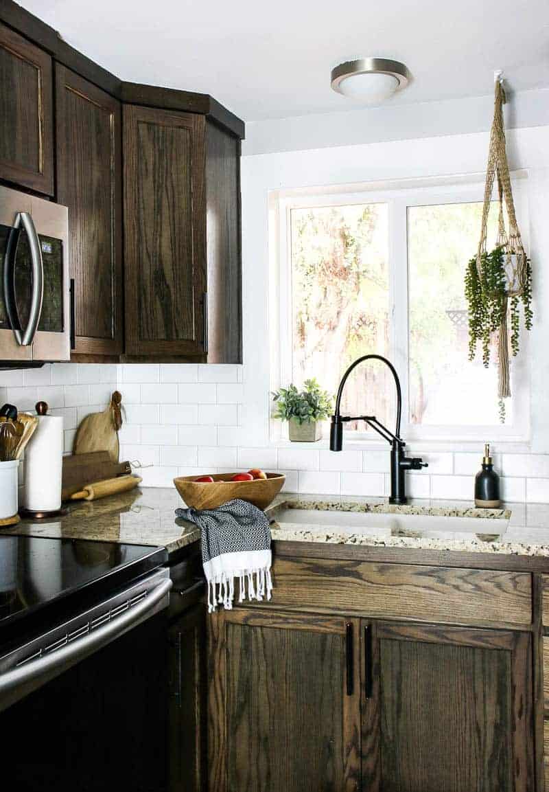 A new farmhouse kitchen sink installed in granite countertops with dark brown cabinets