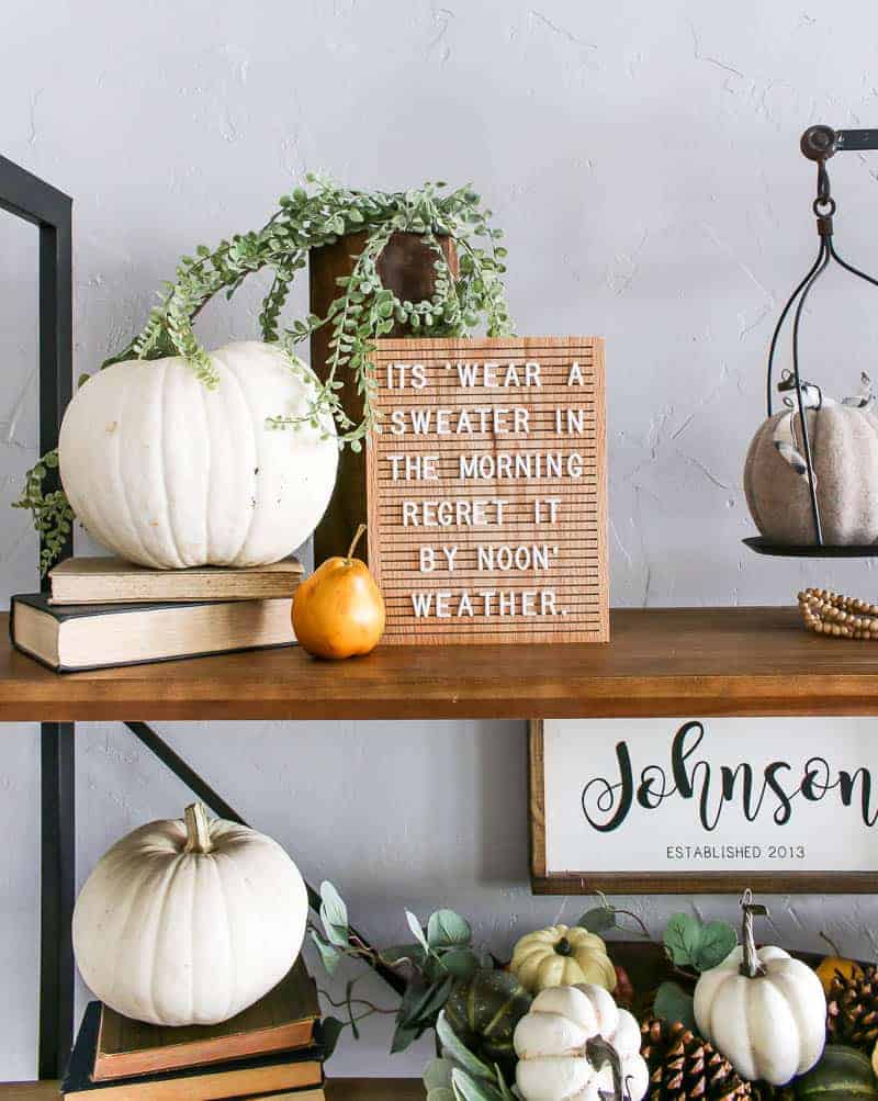 This living room shelf decor is perfect for Fall - a letter board, faux white pumpkin atop stacked vintage books, and faux greenery.