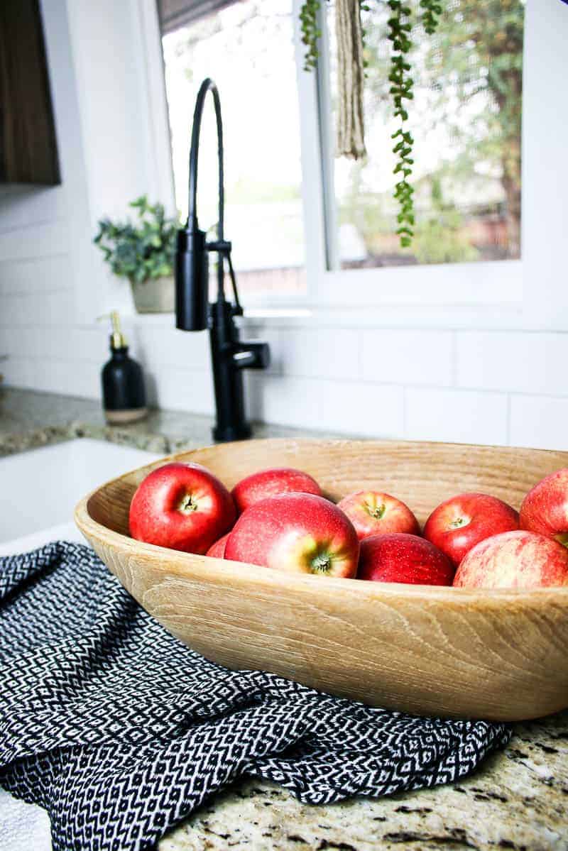 Wooden bowl with apples in front of an undermounted kitchen sink with black faucet in the background