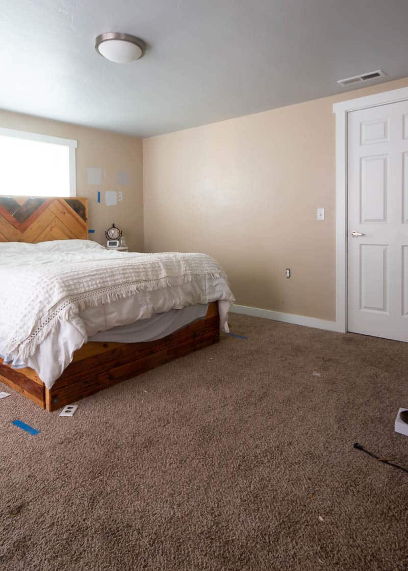 Another view of our master bedroom with a large bed, brown carpet, and tan walls.