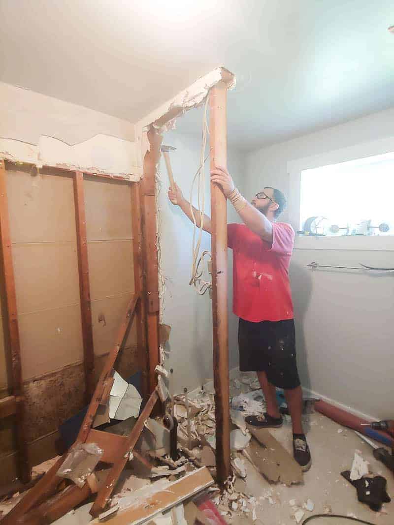 A man is removing the old shower wall using a hammer.