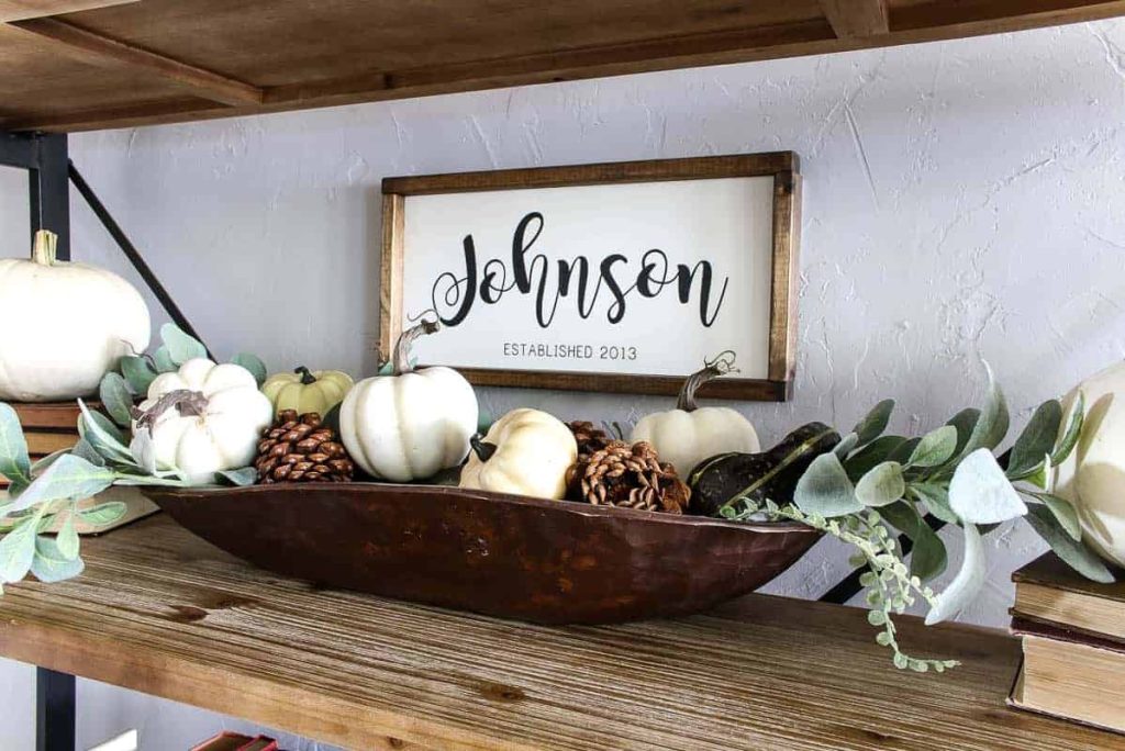 A photo of fall décor showcasing pine cones in a wood dough bowl, with a few mini pumpkins and greenery for easy and inexpensive decoration.