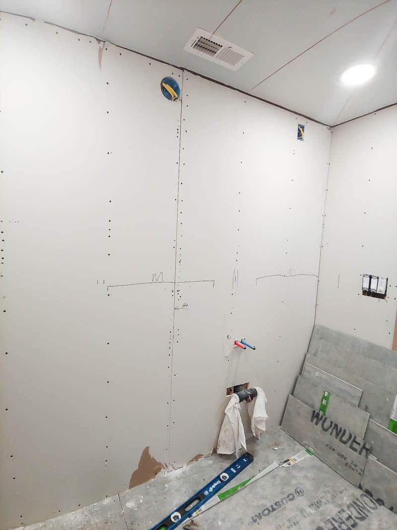 A bathroom wall with plywood is ready for drywall attachment in this bathroom renovation